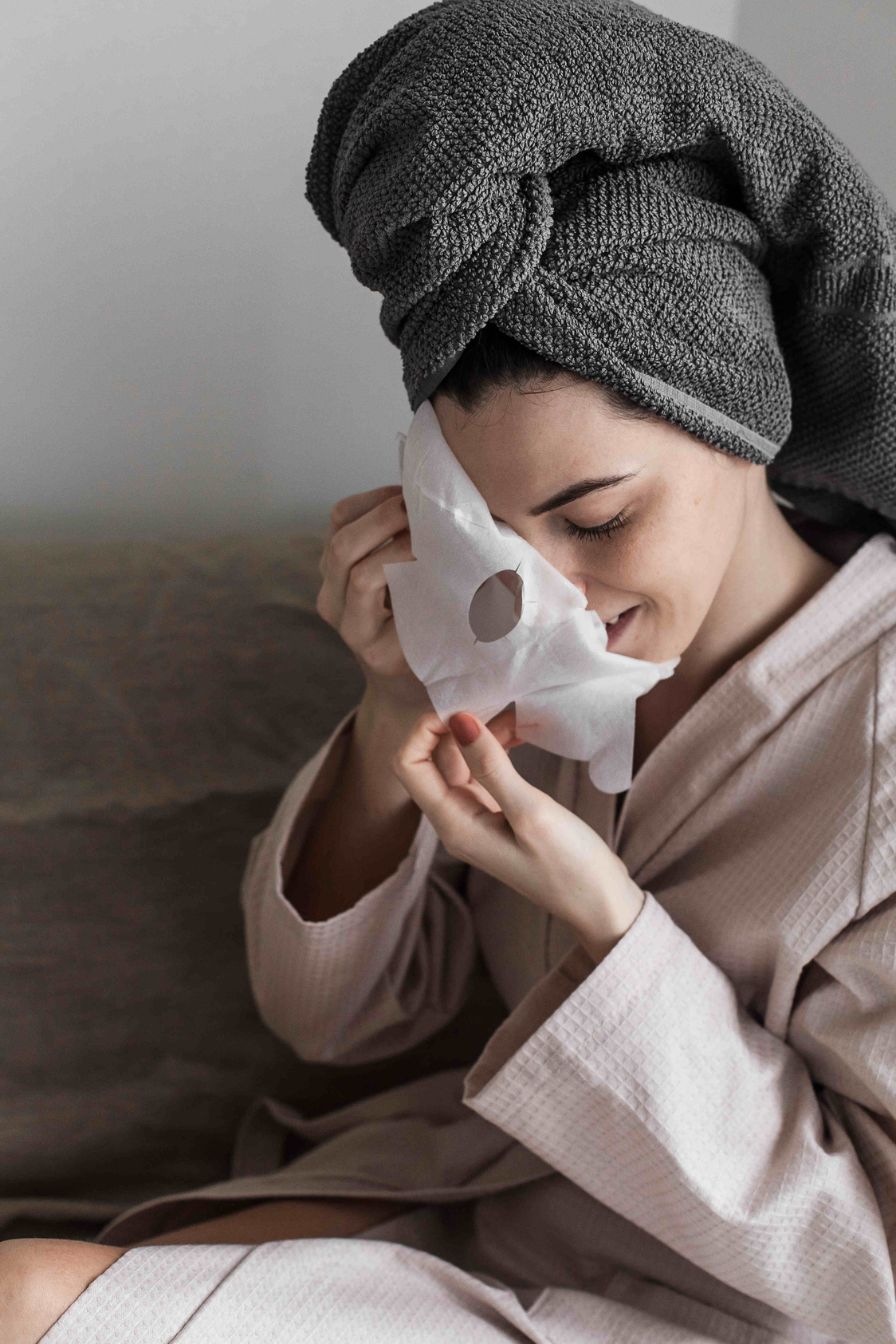 Woman in Bathrobe with Towel on Head Removing Face Mask